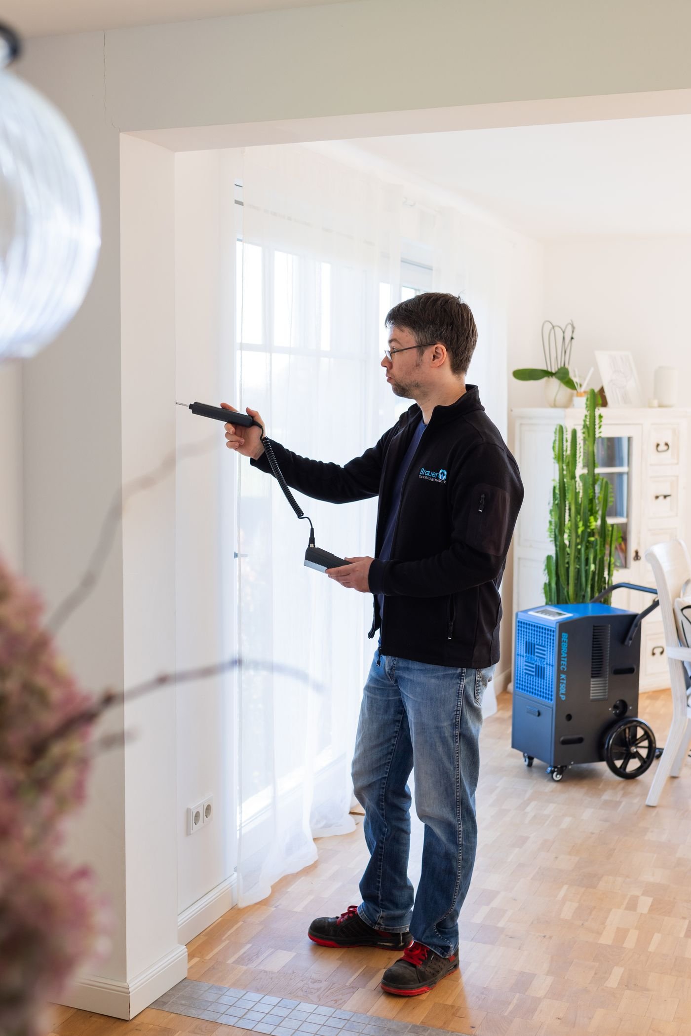 Kondenstrockner läuft im Wohnraum, der Techniker kontrolliert die Wandfeuchte